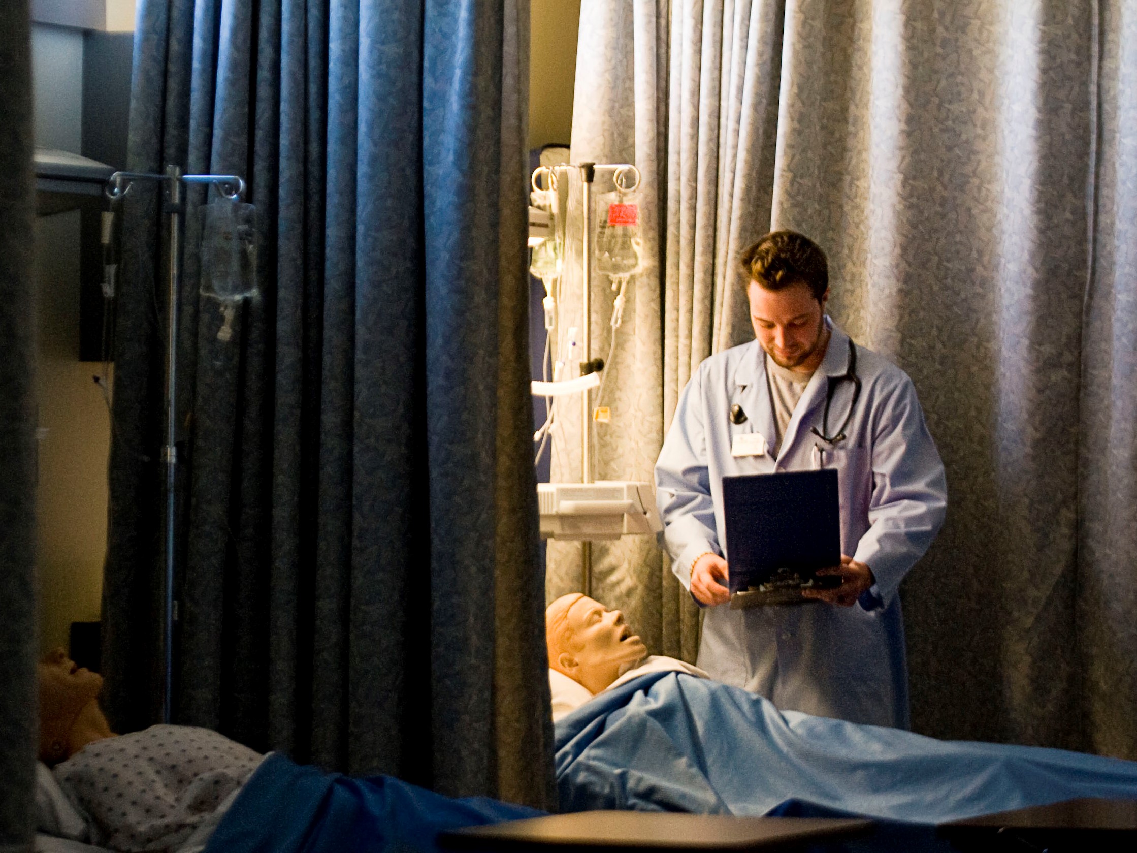 Male nursing student stands over a dummy patient.